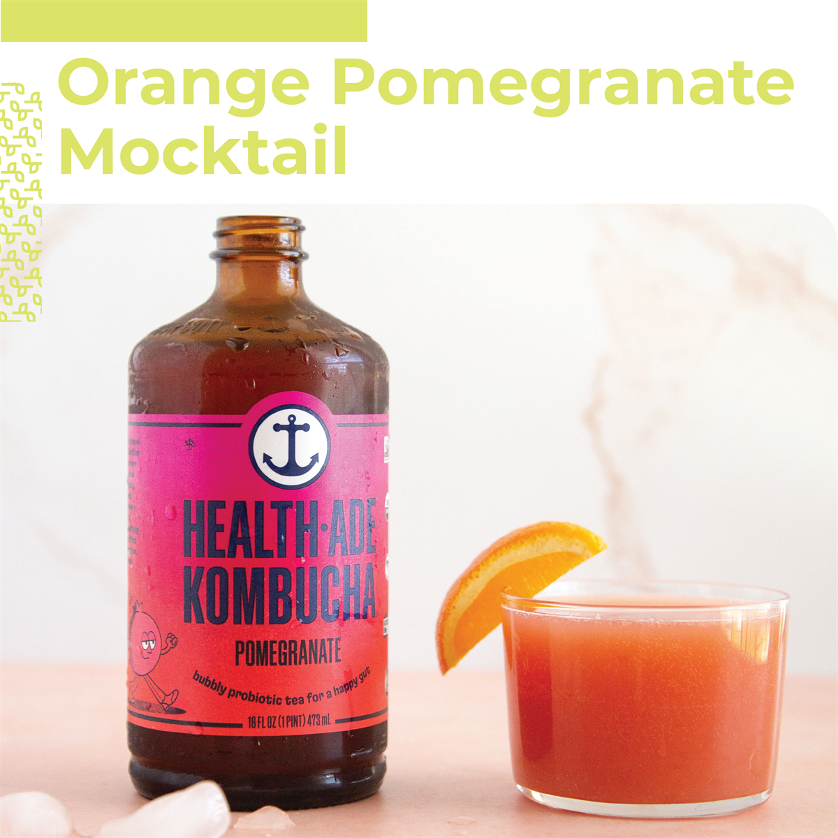 A glass of orange pomegranate mocktail, with an orange slice on the rim, next to a bottle of Health-Ade Pomegranate Kombucha.